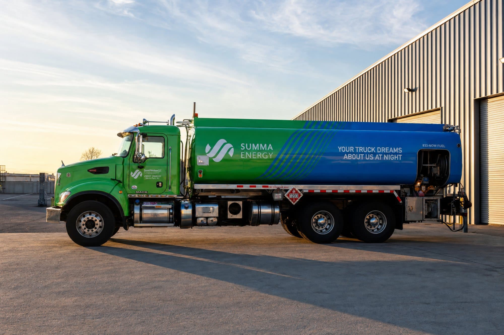 A green and blue Summa tanker parked alongside a depot building in low evening sun.