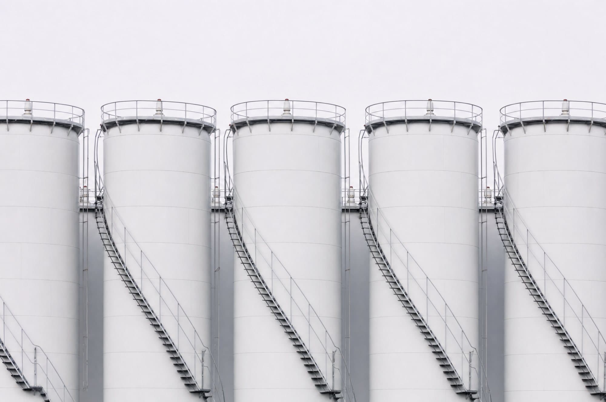A row of tall white bulk storage tanks with external stairways curving around them.
